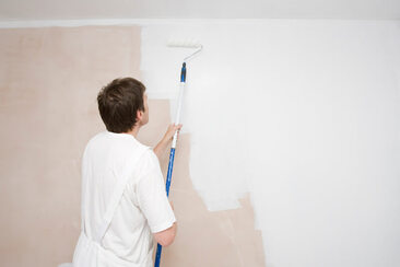 Painter in Ilford using paint roller to apply white paint to wall